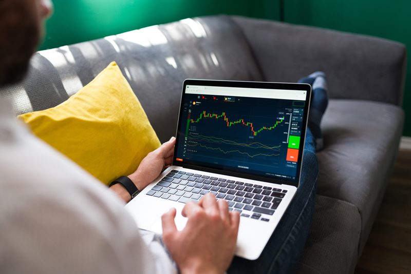 trading-finances-young-man-resting-couch-while-checking-stock-market-laptop